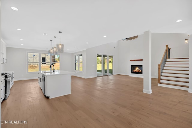 kitchen with a sink, a glass covered fireplace, white cabinetry, stainless steel appliances, and light countertops