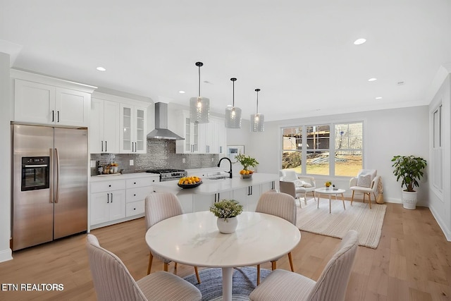 kitchen featuring wall chimney range hood, a center island with sink, decorative backsplash, stainless steel fridge, and a sink