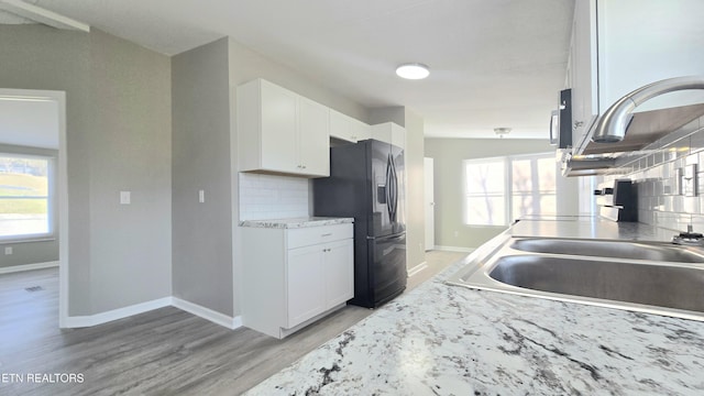 kitchen featuring light stone countertops, black fridge, white cabinets, and light wood-type flooring