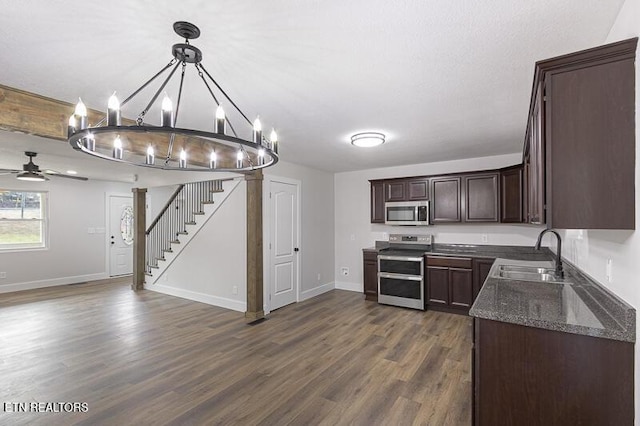 kitchen with pendant lighting, sink, appliances with stainless steel finishes, dark stone countertops, and dark brown cabinets