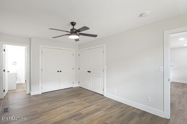 unfurnished bedroom with ceiling fan, connected bathroom, dark hardwood / wood-style floors, and two closets