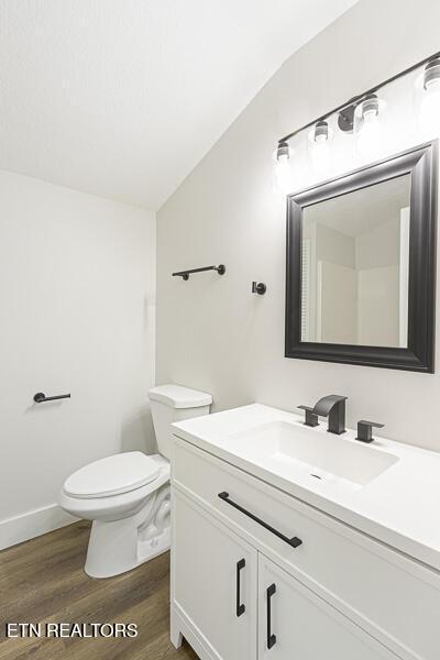 bathroom with hardwood / wood-style flooring, vaulted ceiling, vanity, and toilet