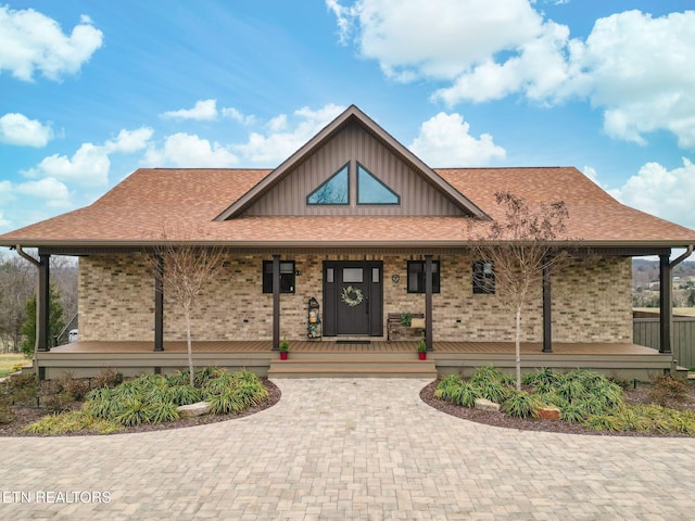 view of front of house with covered porch, brick siding, and roof with shingles