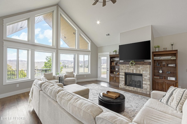 living room featuring high vaulted ceiling, a brick fireplace, wood finished floors, and baseboards