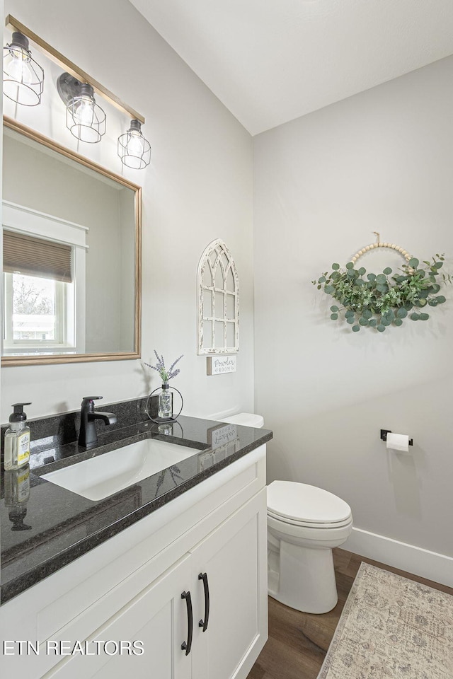 half bath with baseboards, vanity, toilet, and wood finished floors