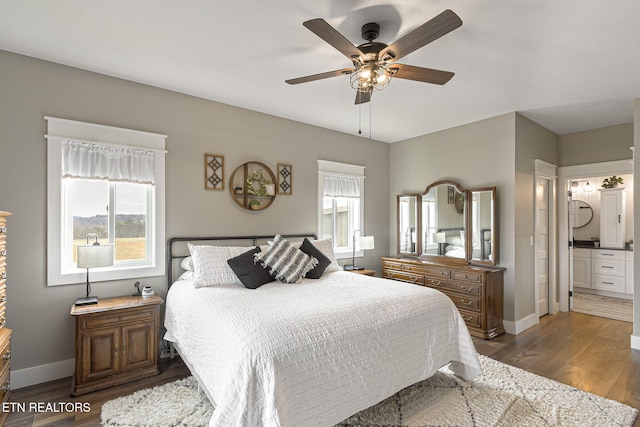 bedroom featuring ceiling fan, baseboards, dark wood-style flooring, and ensuite bathroom