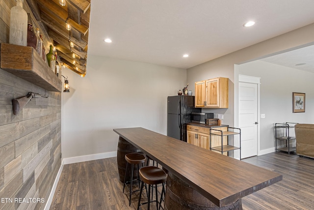 kitchen with dark wood finished floors, dark countertops, stainless steel microwave, freestanding refrigerator, and light brown cabinets