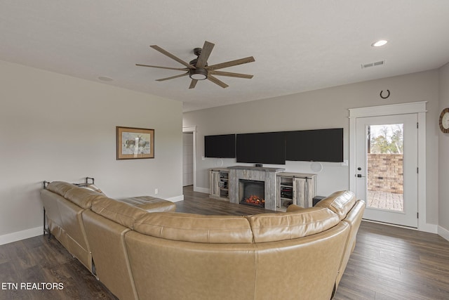 living area with a warm lit fireplace, dark wood-style flooring, visible vents, and baseboards