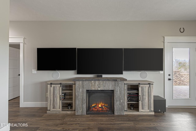 unfurnished living room with dark wood-style floors, a warm lit fireplace, baseboards, and a textured ceiling