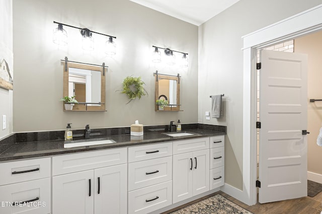 bathroom with double vanity, baseboards, a sink, and wood finished floors