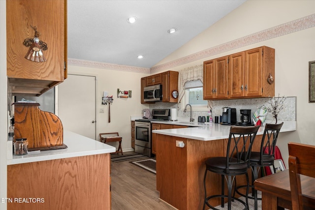 kitchen with lofted ceiling, appliances with stainless steel finishes, brown cabinets, a peninsula, and light countertops