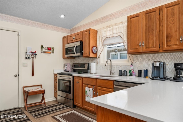 kitchen featuring lofted ceiling, brown cabinets, stainless steel appliances, light countertops, and a sink