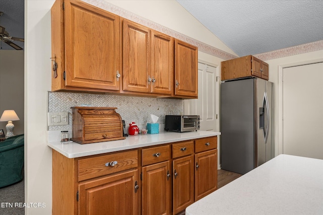 kitchen with brown cabinets, lofted ceiling, light countertops, and stainless steel fridge with ice dispenser