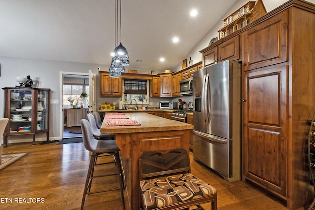 kitchen with a kitchen island, lofted ceiling, hanging light fixtures, stainless steel appliances, and dark wood-type flooring