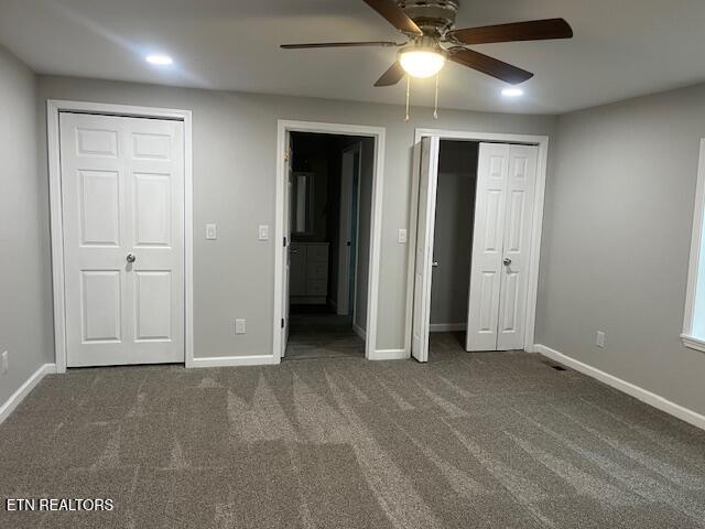 unfurnished bedroom with multiple closets, ceiling fan, and dark colored carpet