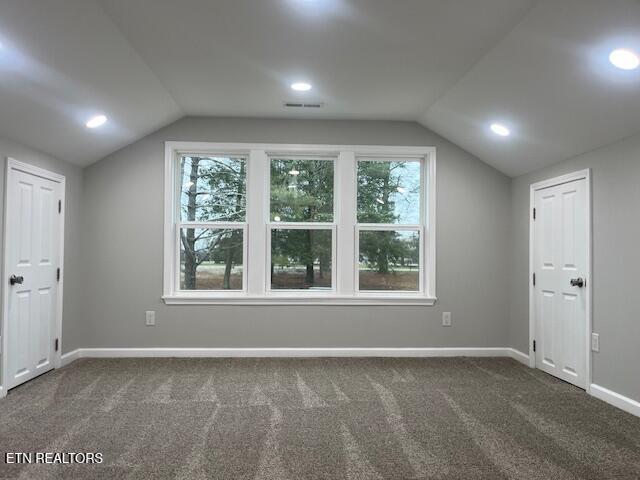 additional living space featuring vaulted ceiling and dark colored carpet