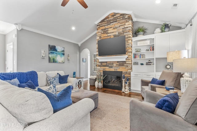 living room with vaulted ceiling, crown molding, dark wood-type flooring, and a stone fireplace