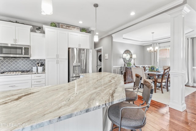 kitchen with white cabinetry, stainless steel appliances, ornate columns, stacked washer / dryer, and pendant lighting