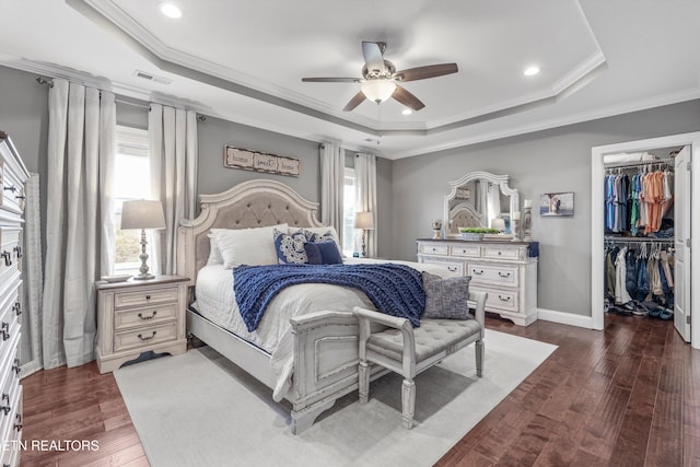 bedroom with a tray ceiling, dark hardwood / wood-style flooring, crown molding, and a spacious closet