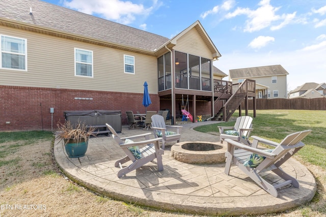 rear view of house with a fire pit, a yard, a hot tub, a patio area, and a sunroom