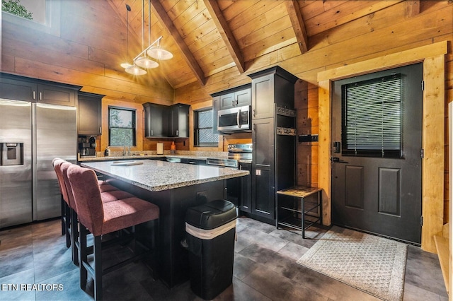 kitchen with light stone counters, decorative light fixtures, a center island, wooden walls, and stainless steel appliances