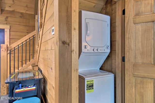 laundry area with stacked washer / drying machine and wood walls