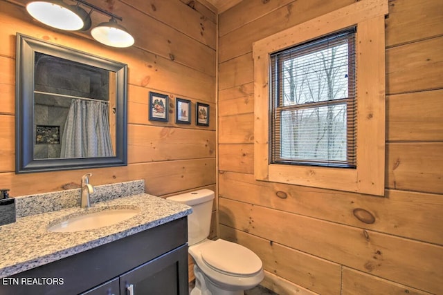 bathroom with vanity, toilet, and wood walls