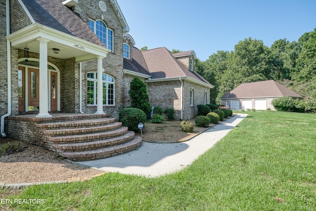 view of side of property featuring a garage, an outdoor structure, covered porch, and a lawn