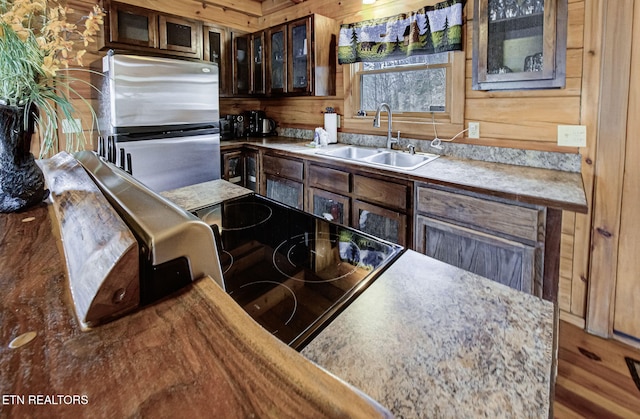 kitchen with dark brown cabinetry, sink, stainless steel refrigerator, wooden walls, and hardwood / wood-style flooring