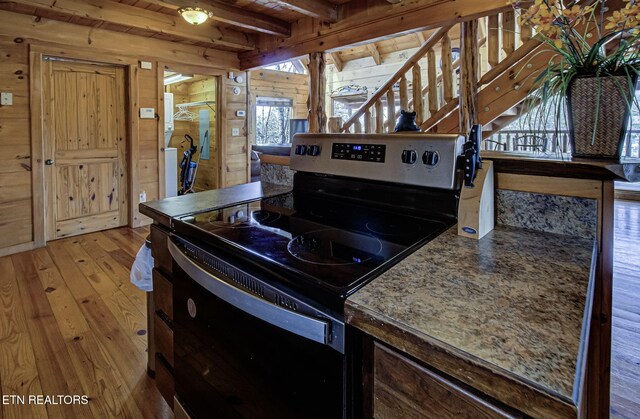 kitchen with wood walls, wooden ceiling, black / electric stove, beamed ceiling, and light hardwood / wood-style floors