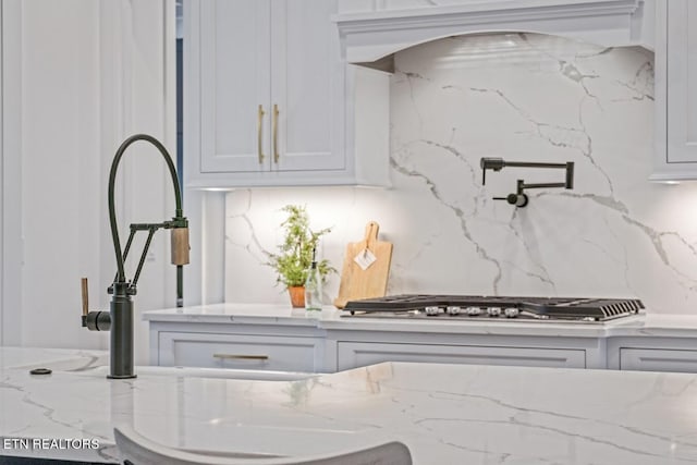 kitchen featuring stainless steel gas cooktop, exhaust hood, light stone countertops, decorative backsplash, and white cabinets