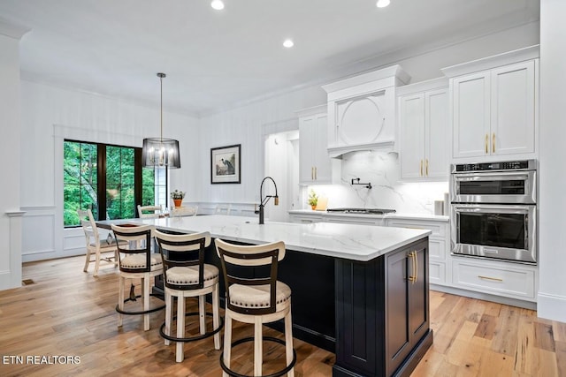 kitchen featuring light stone counters, stainless steel appliances, a kitchen island with sink, and white cabinets