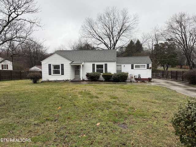 ranch-style home featuring a front lawn, roof with shingles, and fence