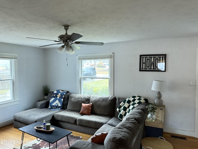 living area featuring a textured ceiling, wood finished floors, a ceiling fan, visible vents, and baseboards