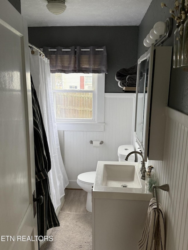 full bathroom with a textured ceiling, curtained shower, toilet, a wainscoted wall, and vanity