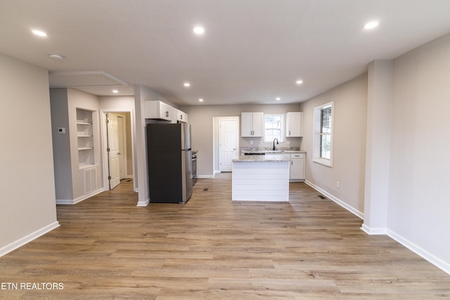 kitchen featuring sink, white cabinetry, a center island, stainless steel fridge, and light hardwood / wood-style floors