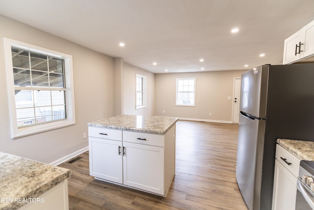 kitchen with light stone counters, stainless steel appliances, a center island, and white cabinets