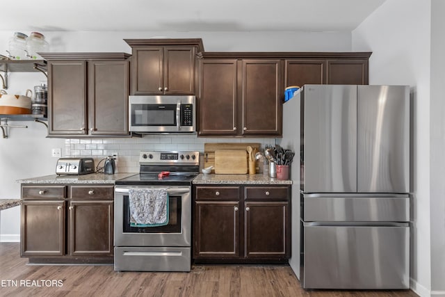 kitchen with light stone counters, dark brown cabinetry, wood finished floors, appliances with stainless steel finishes, and tasteful backsplash