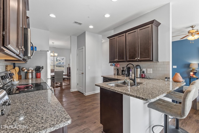 kitchen with dark brown cabinetry, visible vents, appliances with stainless steel finishes, light stone countertops, and a sink