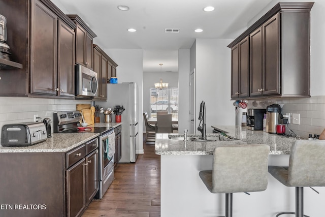 kitchen featuring dark brown cabinetry, a sink, visible vents, appliances with stainless steel finishes, and dark wood-style floors