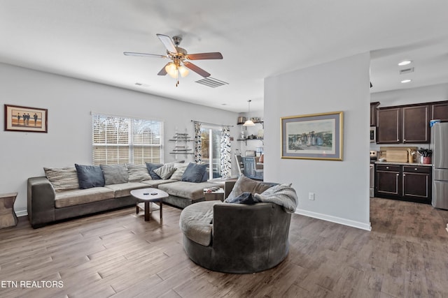 living room with baseboards, wood finished floors, visible vents, and a ceiling fan