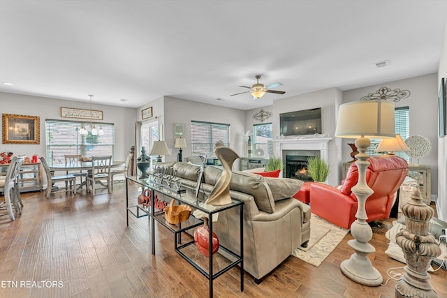 living room featuring a ceiling fan, a lit fireplace, visible vents, and wood finished floors