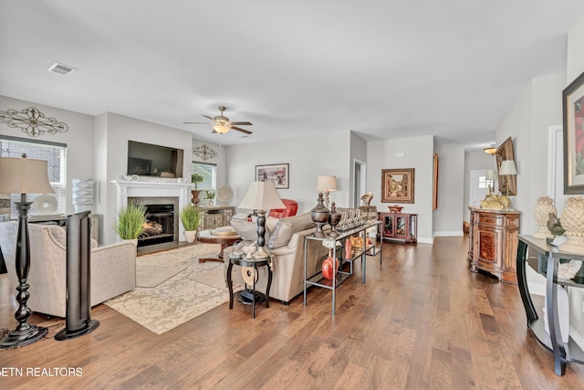 living area featuring a healthy amount of sunlight, a fireplace with flush hearth, visible vents, and wood finished floors