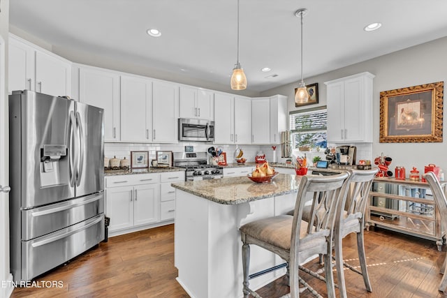 kitchen with light stone countertops, stainless steel appliances, white cabinets, a center island, and decorative light fixtures