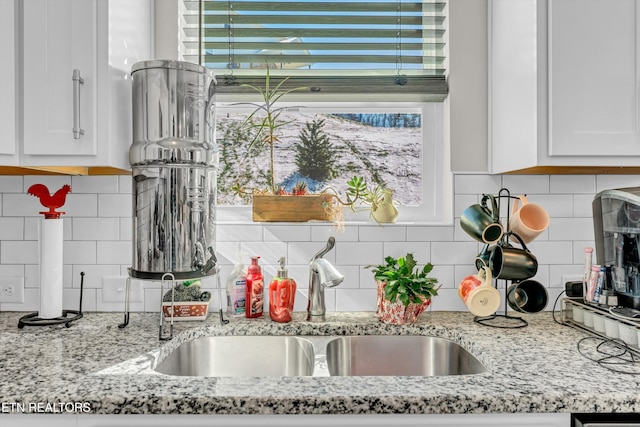 kitchen featuring light stone countertops, backsplash, white cabinets, and a sink