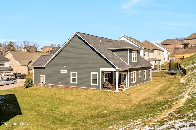 rear view of property with a trampoline, a residential view, a lawn, and a shingled roof