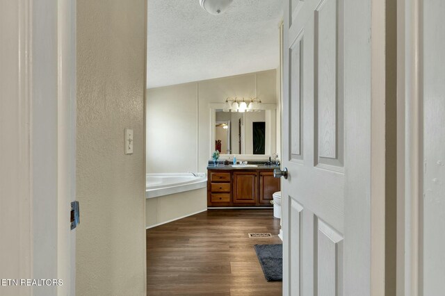 bathroom featuring toilet, a textured ceiling, vanity, a bathing tub, and hardwood / wood-style flooring