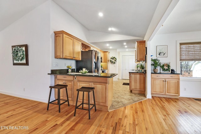 kitchen with light wood finished floors, stainless steel fridge with ice dispenser, lofted ceiling, a kitchen breakfast bar, and a peninsula