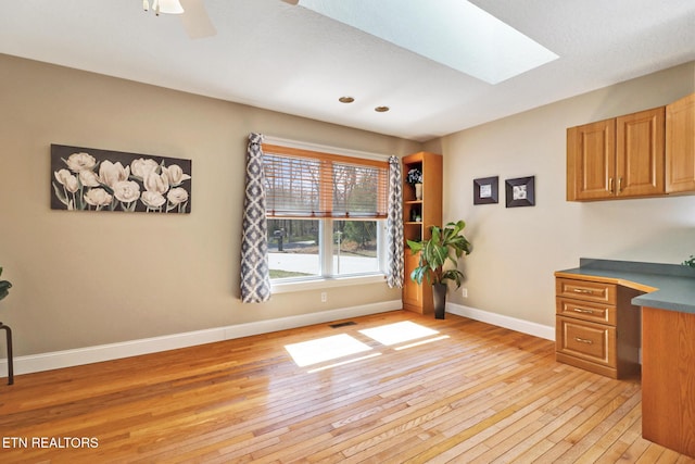 home office with a skylight, baseboards, visible vents, ceiling fan, and light wood-style floors