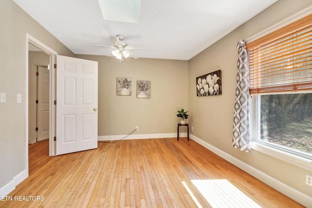 empty room with ceiling fan, light wood-type flooring, a skylight, and baseboards